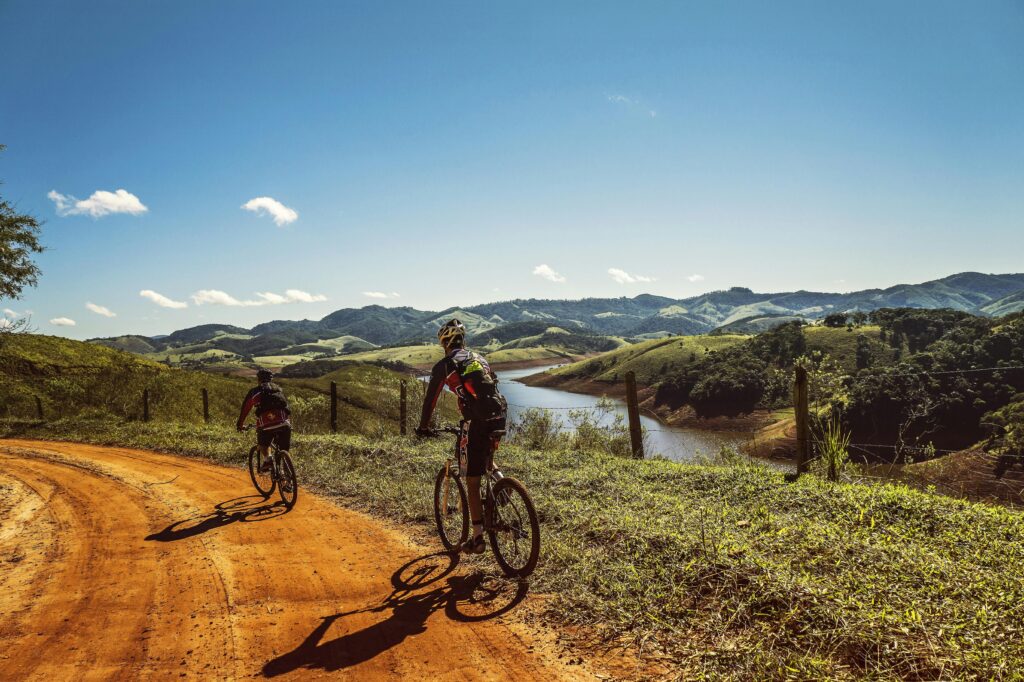 Two cyclists riding on a dirt trail with stunning mountain views and clear skies.